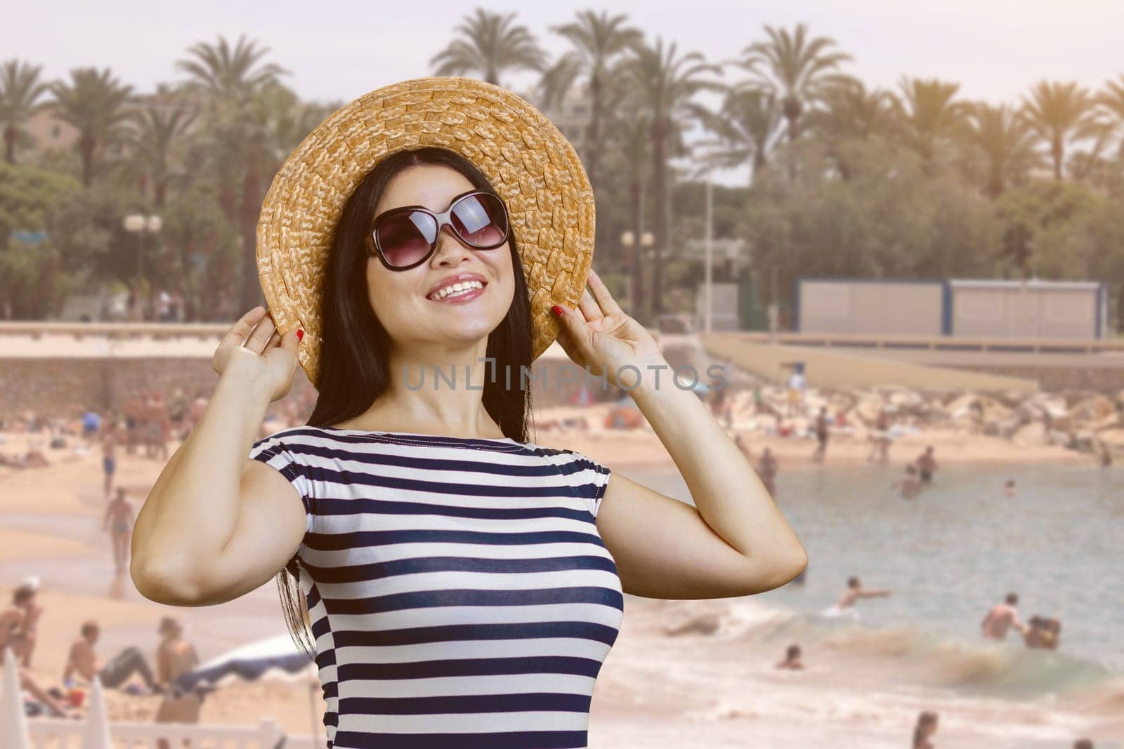 Happy young woman with straw hat standing outdoors. Beach resort background.