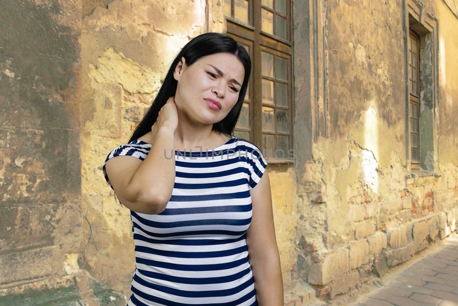 Asian woman is suffering from nechache outdoors. Old shappy house on the background.
