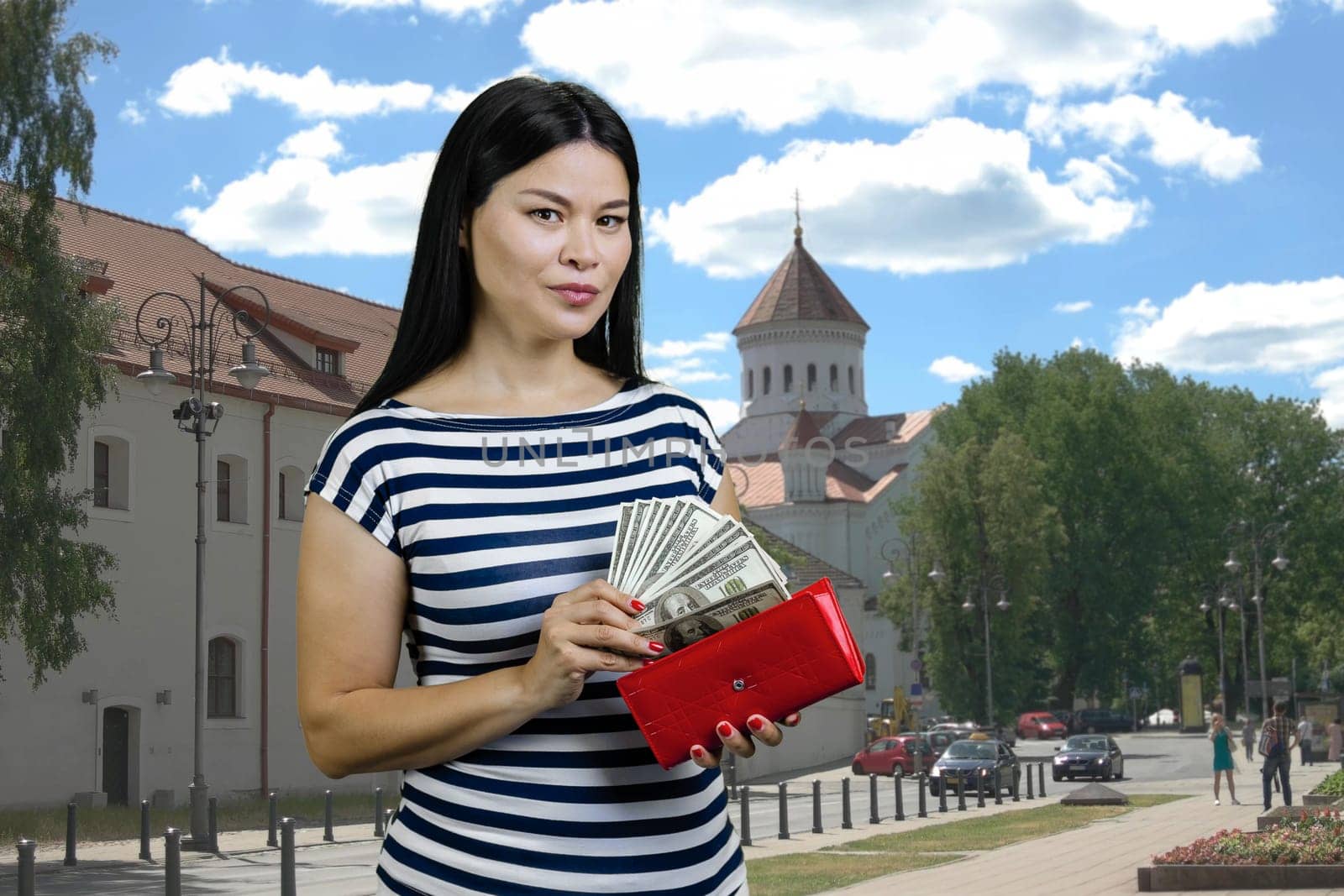 Asian woman with red wallet and dollars. Standing outdoors on the street.