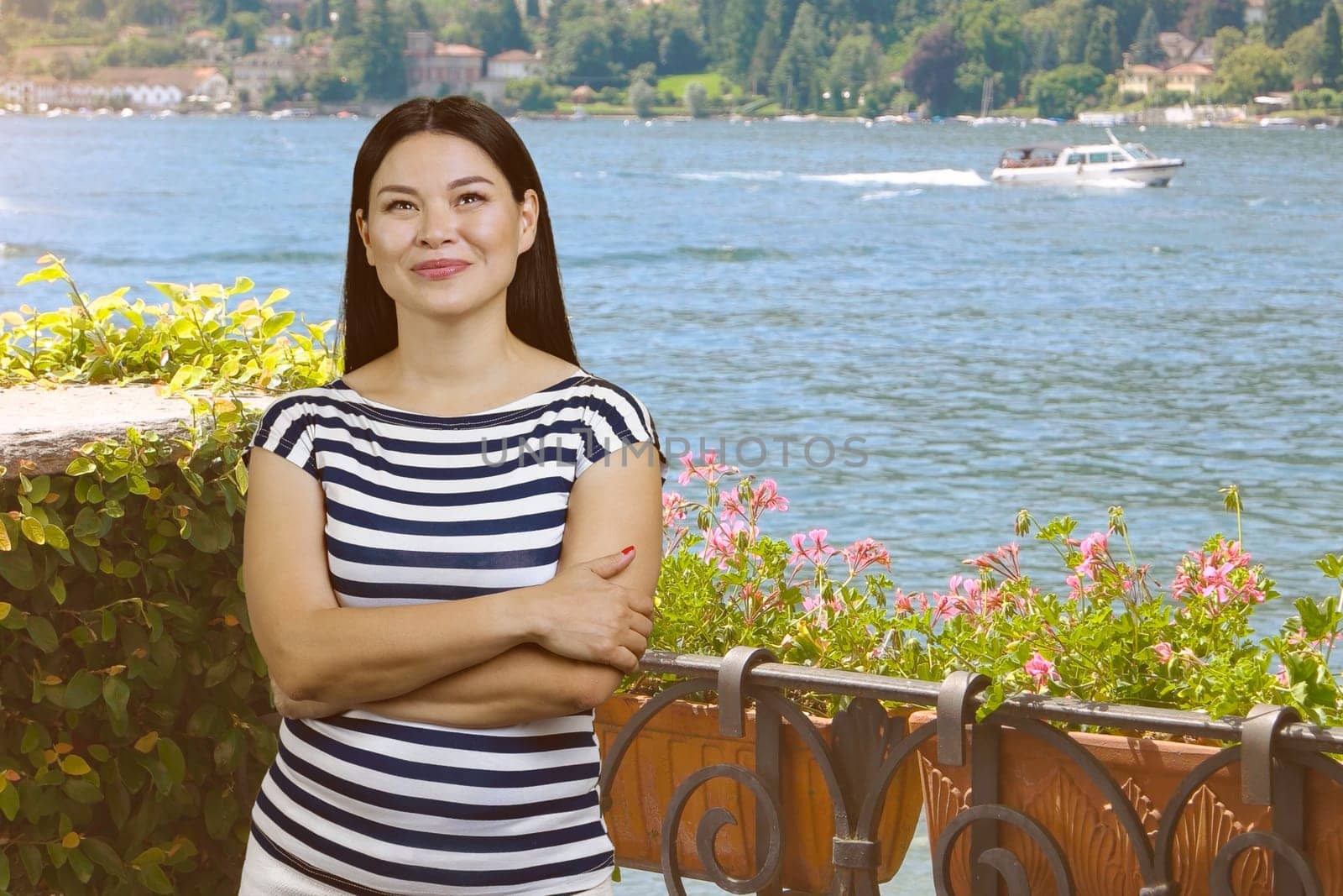 Young asian woman with folded arms standing outdoors. Garden and sea water background.