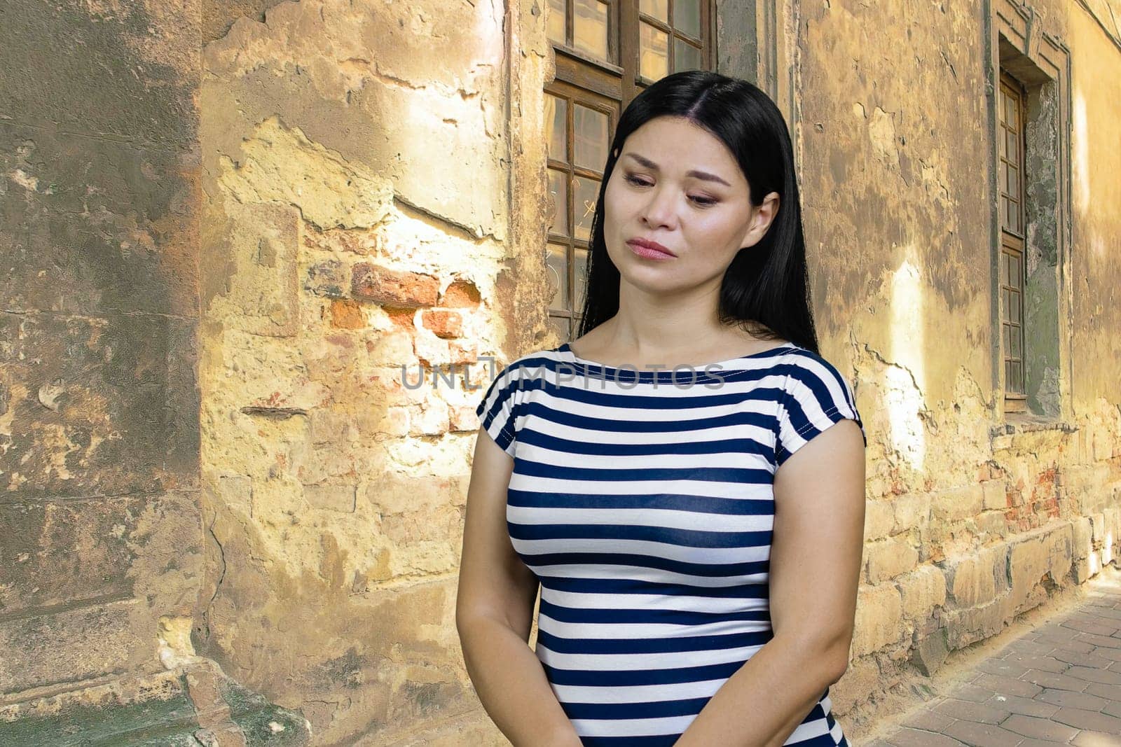 Young pensive sad woman of Asian ethnicity. Shabby building background.