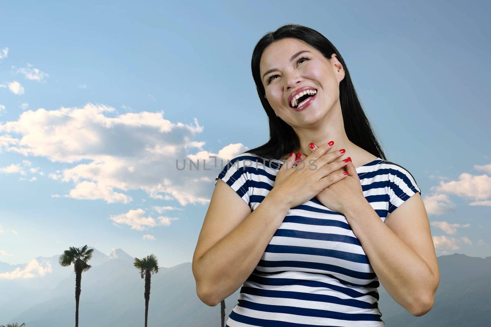 Young asian brunette woman is laughing hard standing outdoors. Blue sky background.