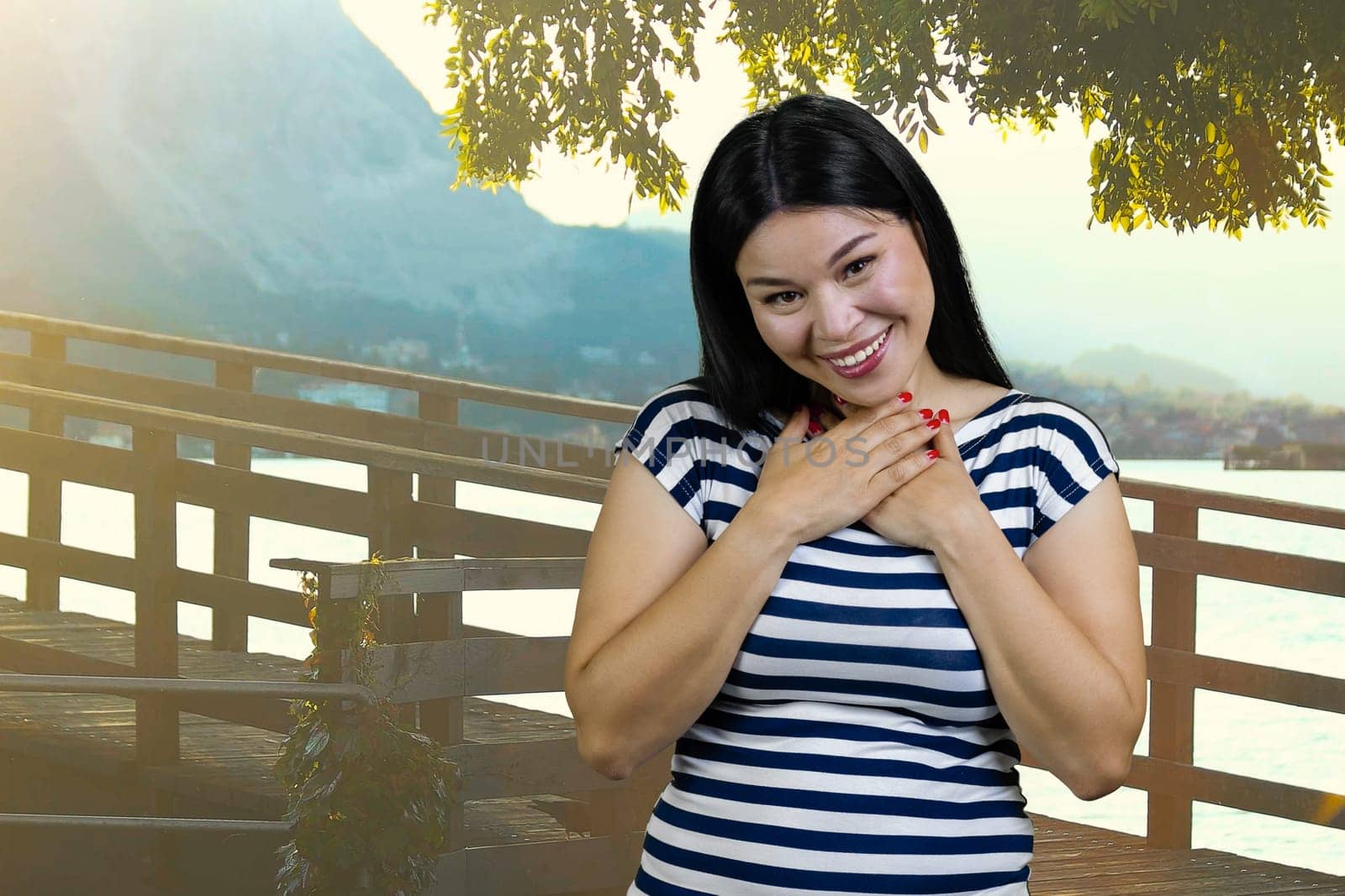 Young asian brunette woman is laughing hard touching her chest with both hands. Summer resort background.