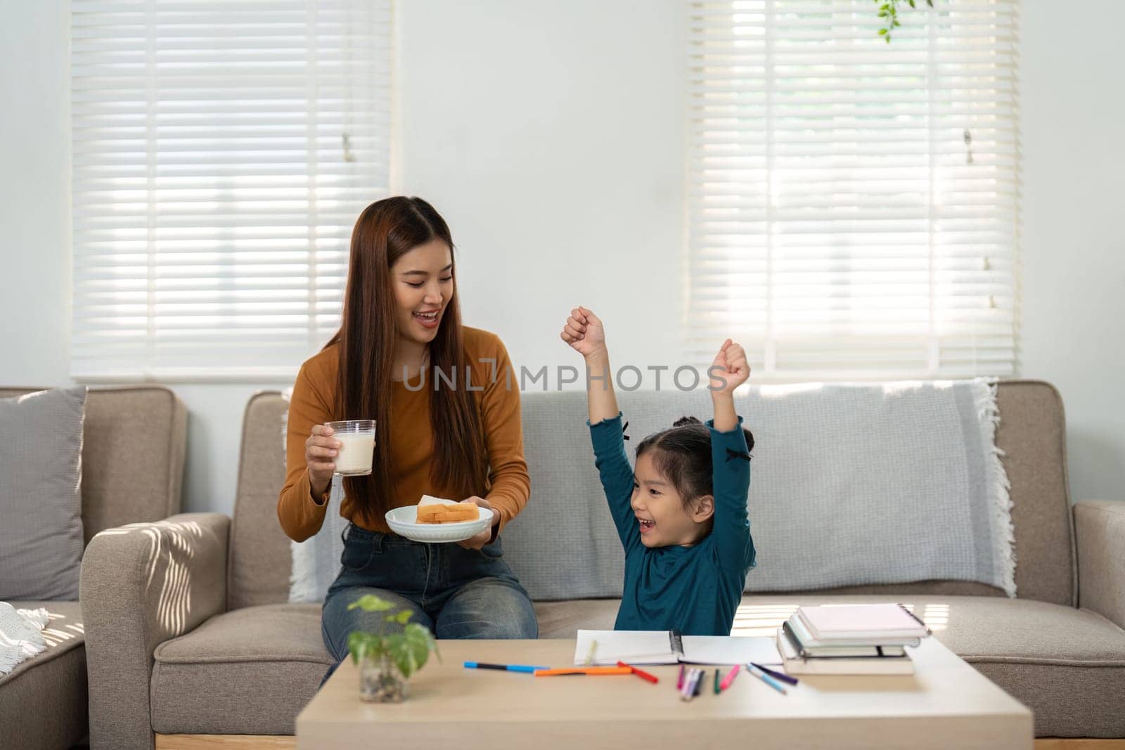 A young girl joyfully raises her arms in celebration as a woman presents snacks, showcasing the joy of learning moments.