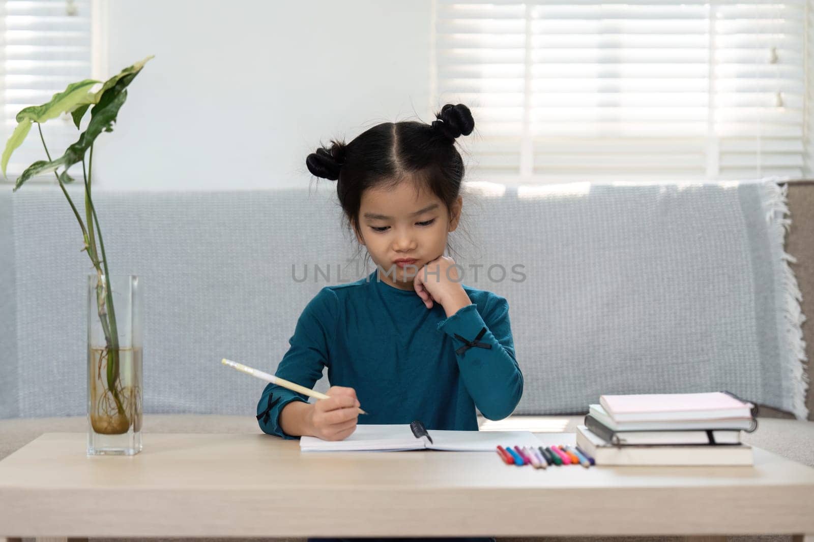 Engaged in her studies, a girl thoughtfully writes in her notebook, symbolizing creativity and concentration in her academic endeavors.