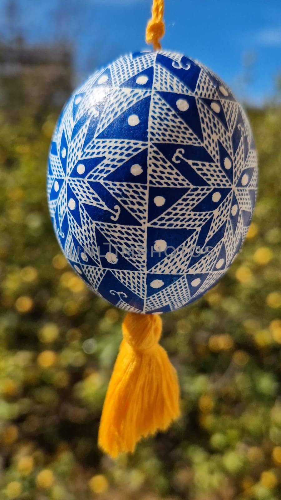 Celebrating traditional Easter, this Ukrainian pysanka features detailed patterns in blue and white. The colorful egg hangs against a backdrop of blooming nature, symbolizing the joy of the season.