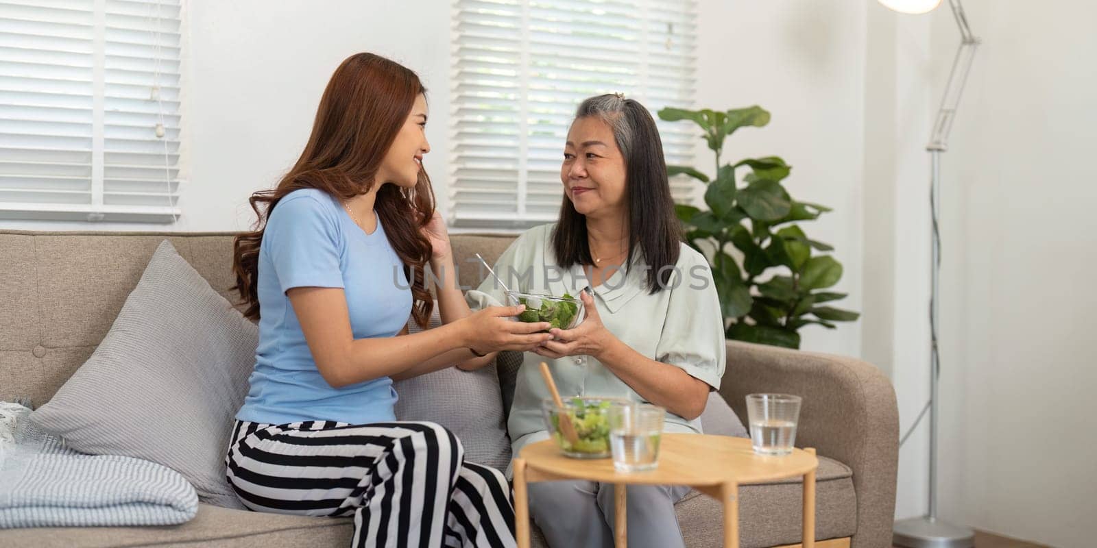 The mother and daughter share a bowl of salad, reveling in the joy of healthy eating and the strong bond they share, highlighting a lifestyle of wellness at home.