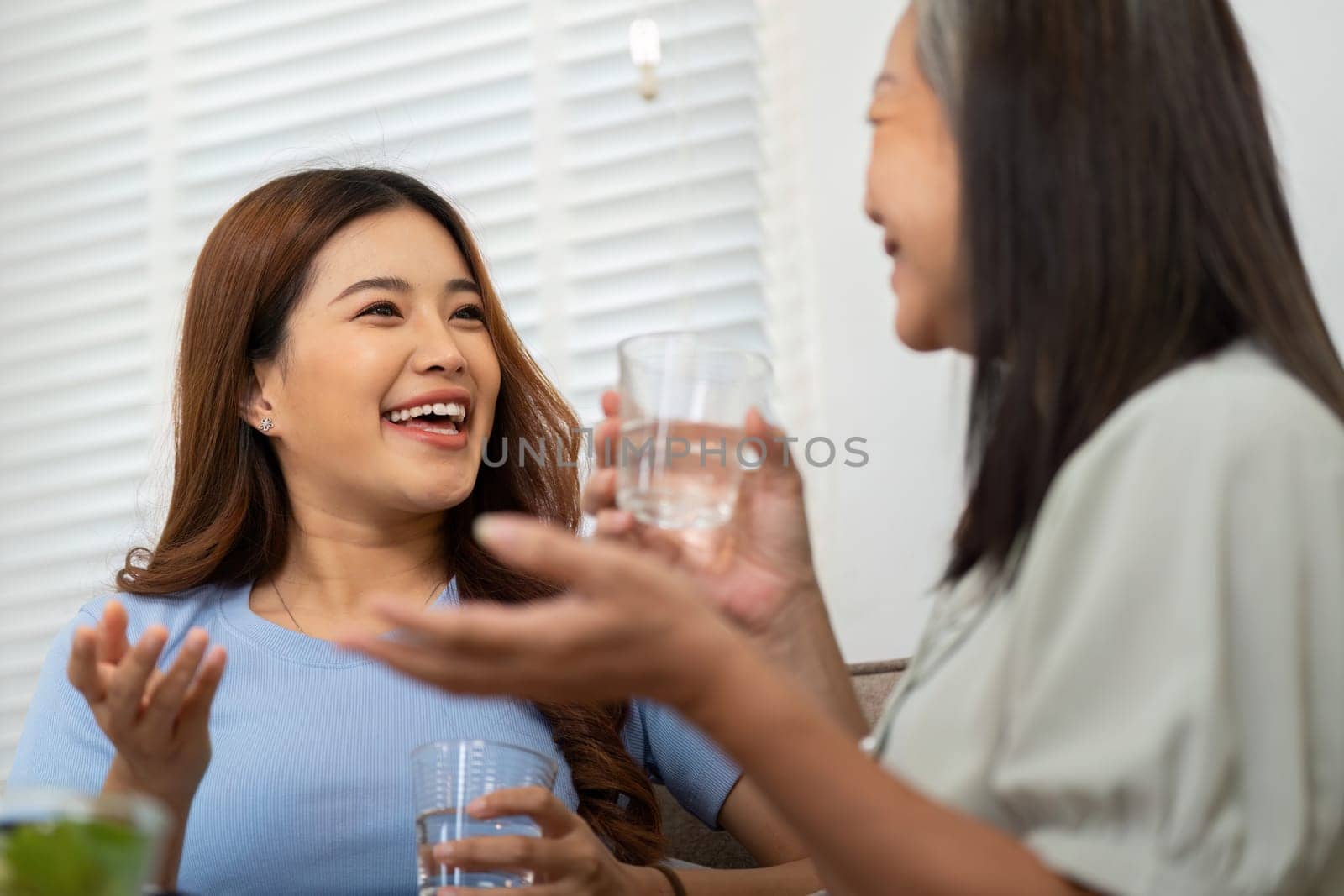 While discussing their day, a mother and daughter raise their glasses in a toast, enjoying water together. Their laughter reflects the essence of social wellness.