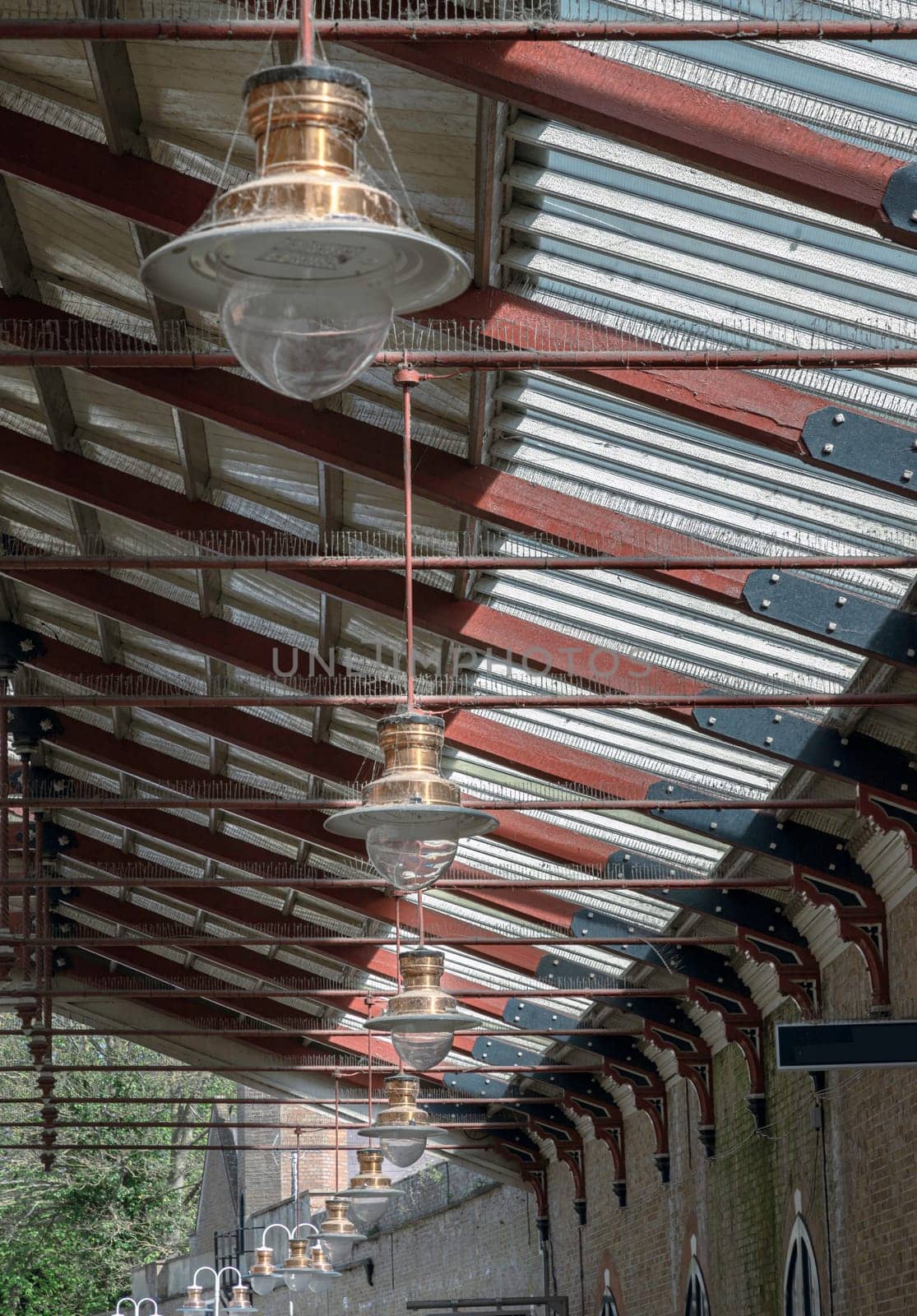 Windsor, England - Apr 03, 2025 - A vintage copper ceiling light fixture with a glass globe shade hangs from a white ceiling and Wooden beams are visible creating a rustic yet elegant interior atmosphere at Windsor & Eton Riverside railway station. Paddington pendant light, use it as your Wallpaper, Poster and Copy space, Selective focus.