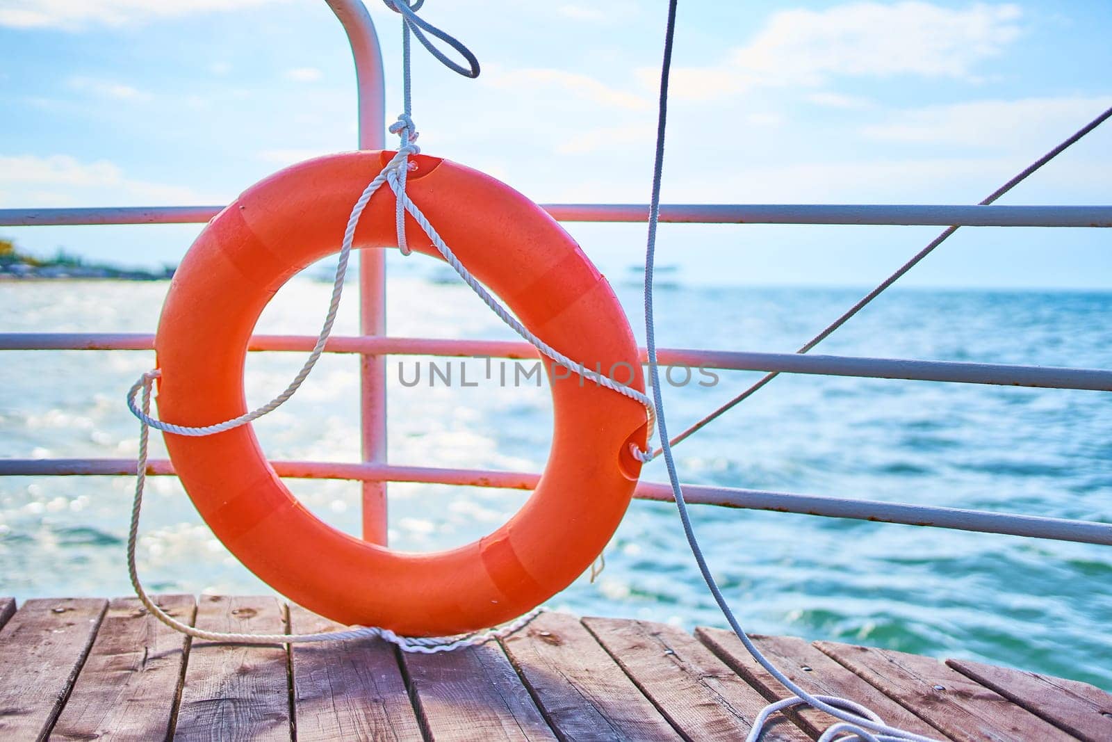 Orange lifebuoy with rope on a wooden pier near sea. Close up of lifebuoy on wooden pier at the beach.
