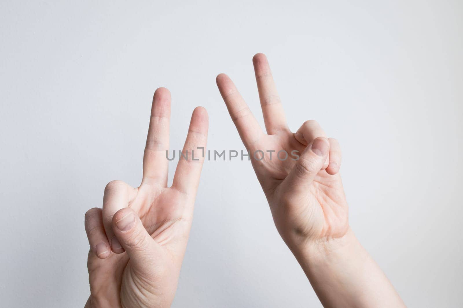 Caucasian hands displaying peace sign gestures against light background.