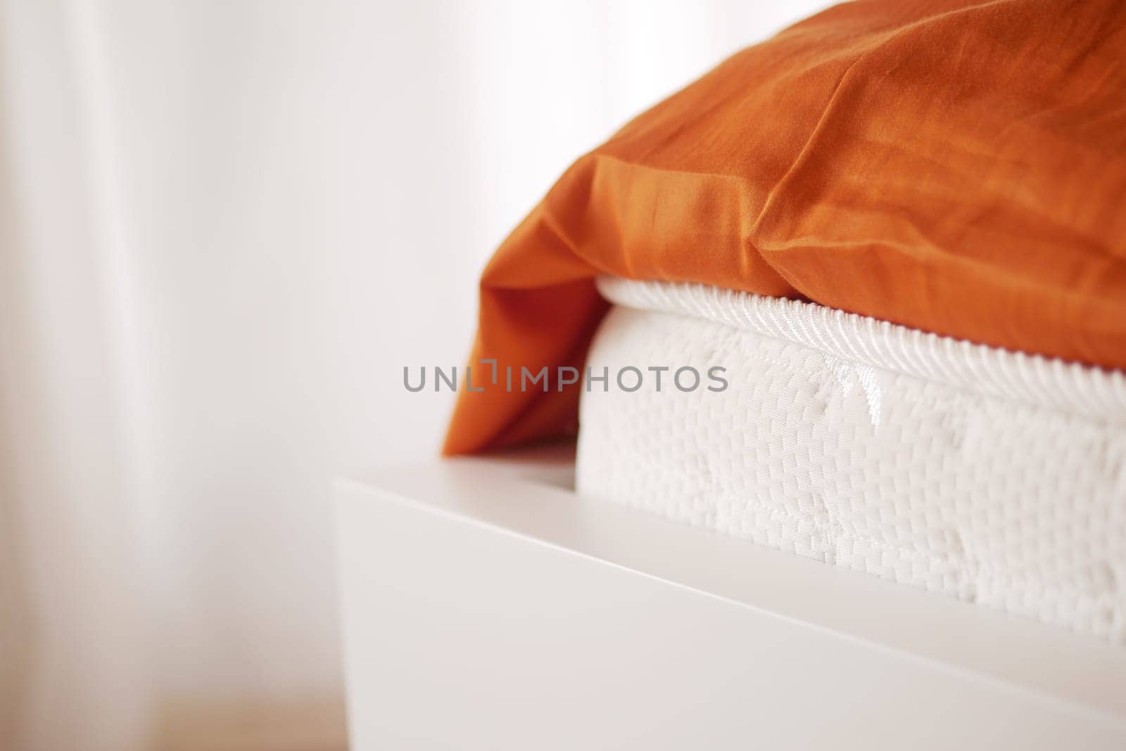A close-up view of a white mattress with an orange blanket draped over it.