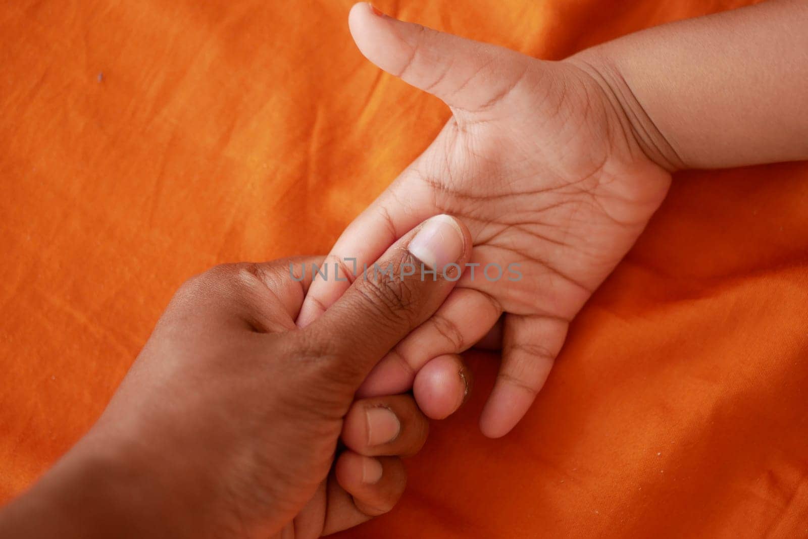 A hand of an adult holds the hand of a child against an orange background.