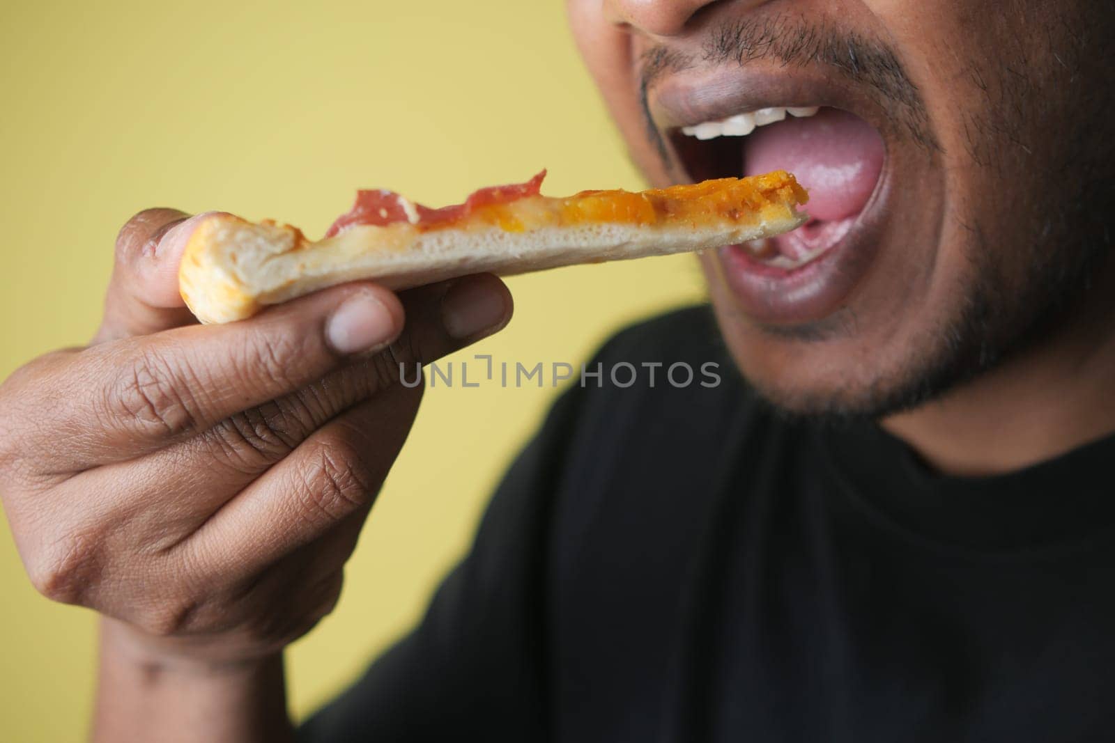 Man takes a bite of pizza slice topped with cheese and meat.