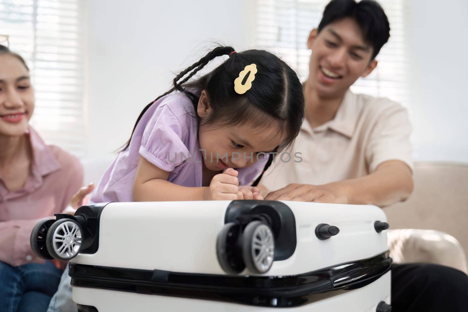 A young girl enjoys her time discovering a suitcase while her father and mother support her, reflecting a lively family atmosphere filled with laughter.