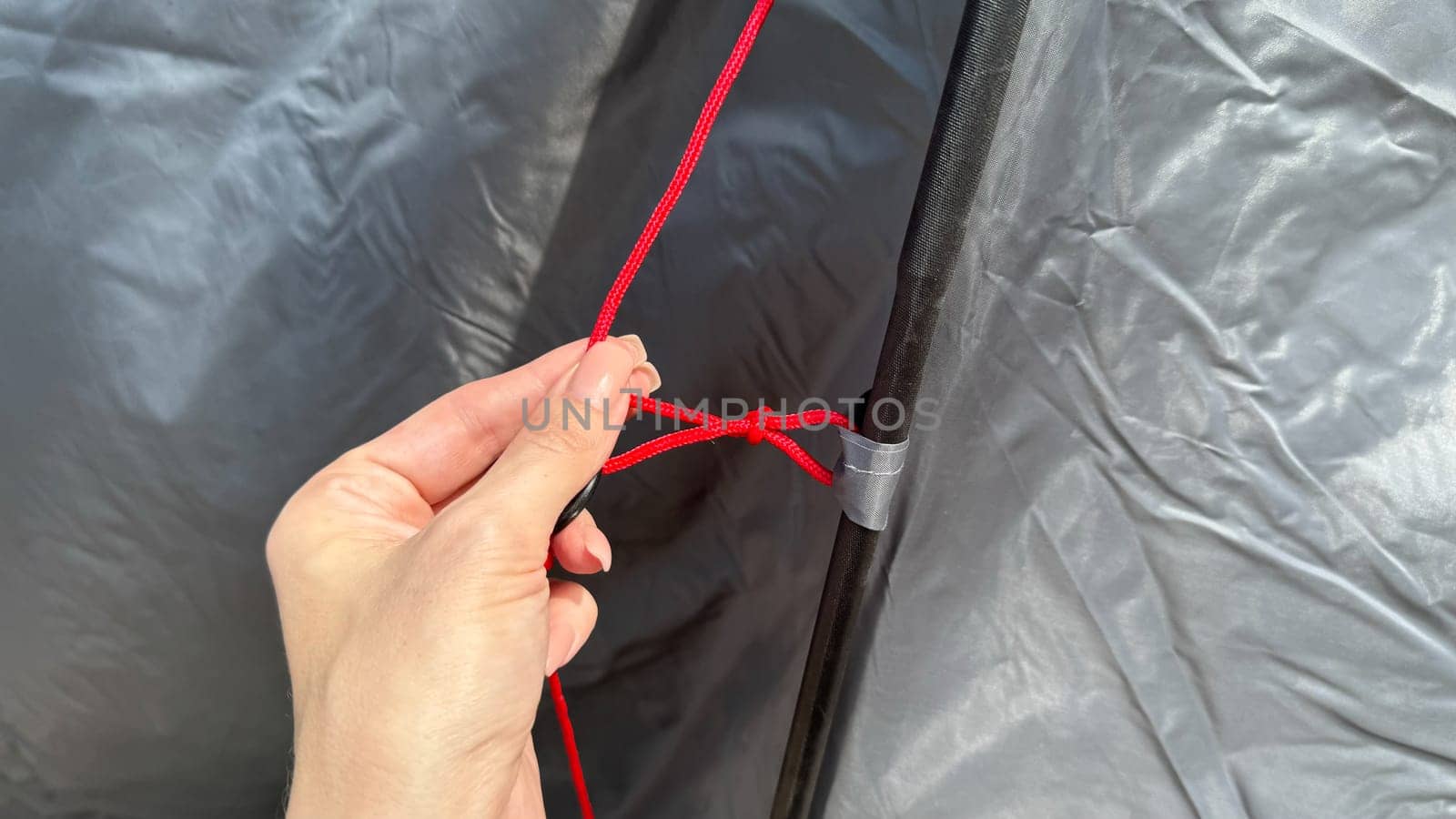 Close-up of a person's hand gripping tent ropes while setting up a tent outdoors. Camping equipment and temporary shelter installation