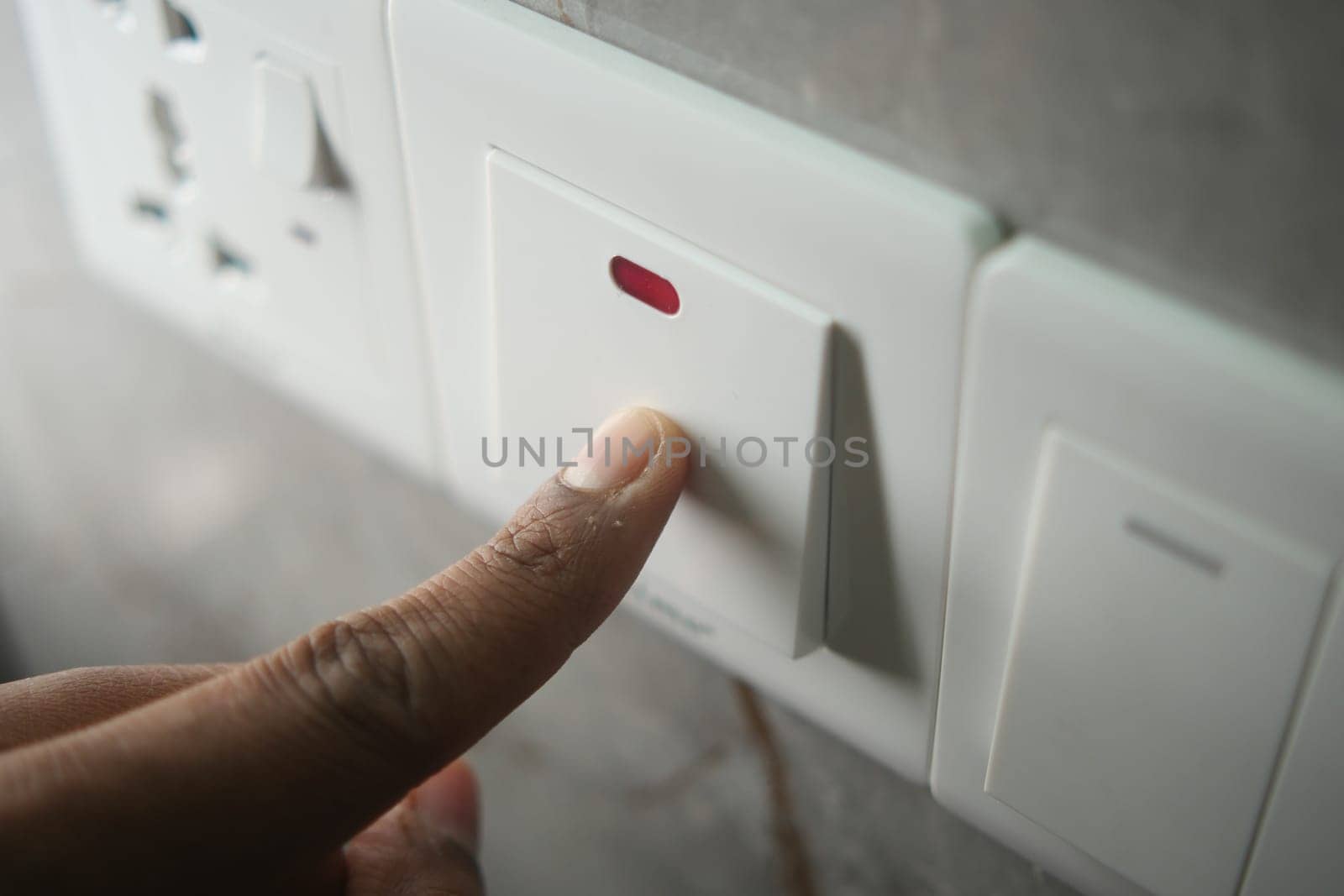A hand presses a modern light switch on a wall, controlling lighting.