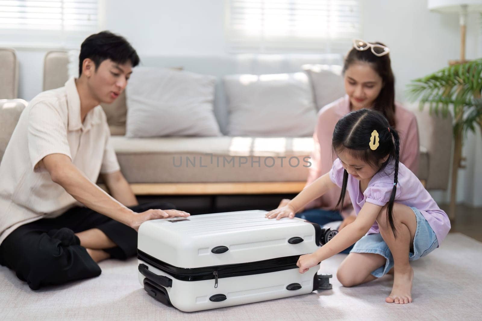 In a cozy living room, a young girl and her parents happily prepare their suitcase for a family vacation, fostering a sense of adventure and connection.