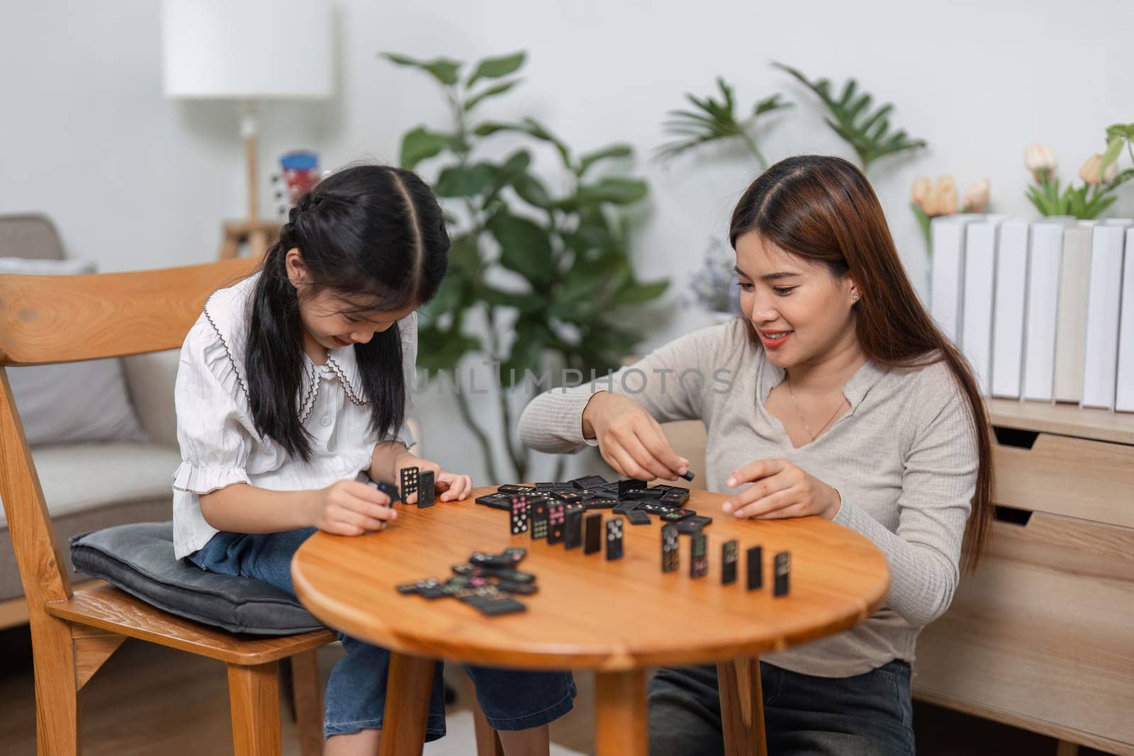The excitement builds as a mother and daughter strategize during their domino game, highlighting the importance of family relationships in playful scenarios.