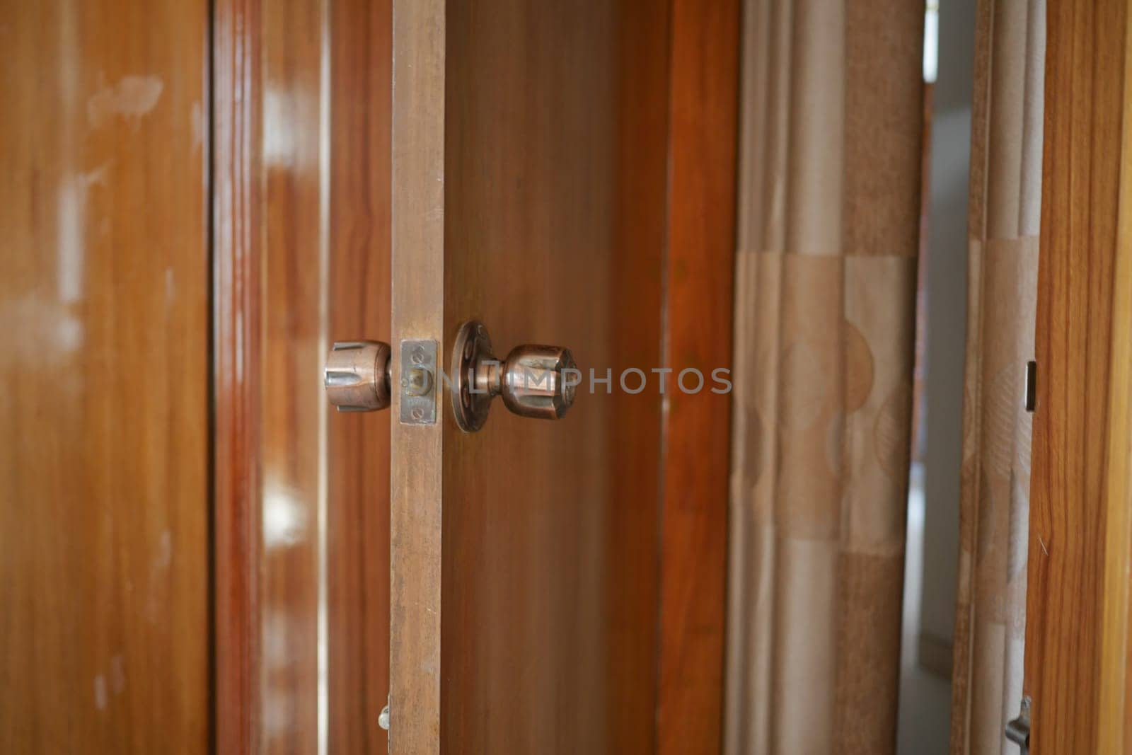 A wooden cabinet door partially open, showing a shiny knob and rich grain.