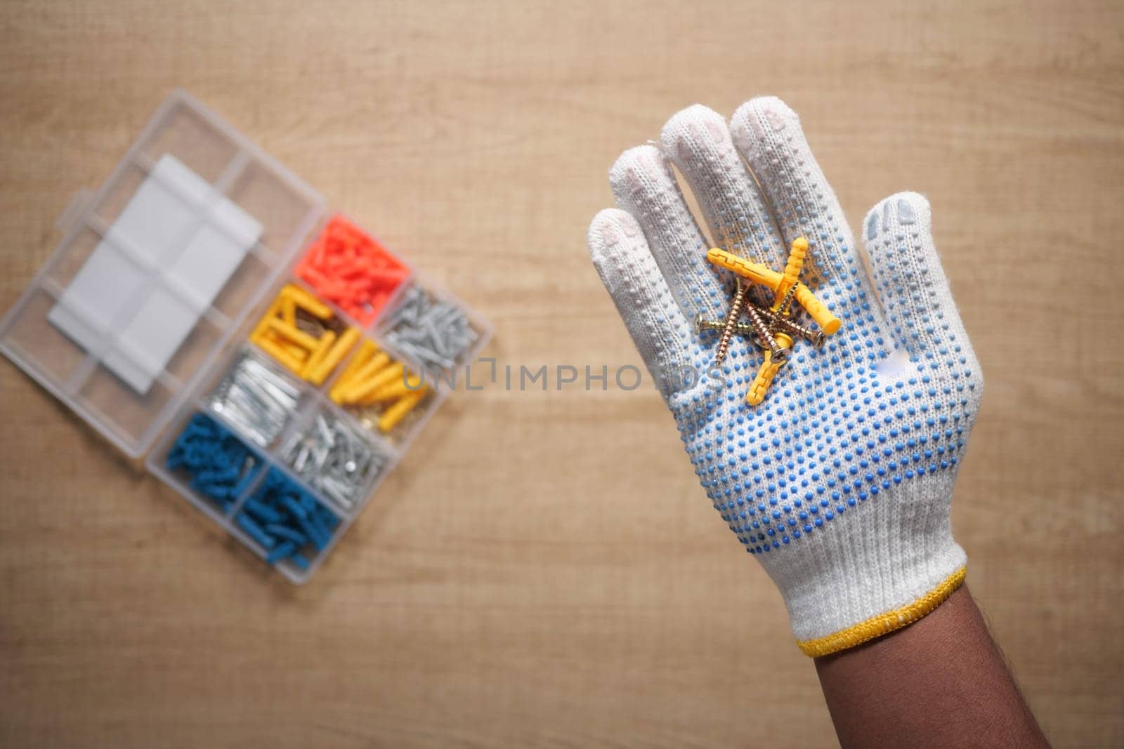 A worker in safety gloves holds screws while a toolbox is visible.