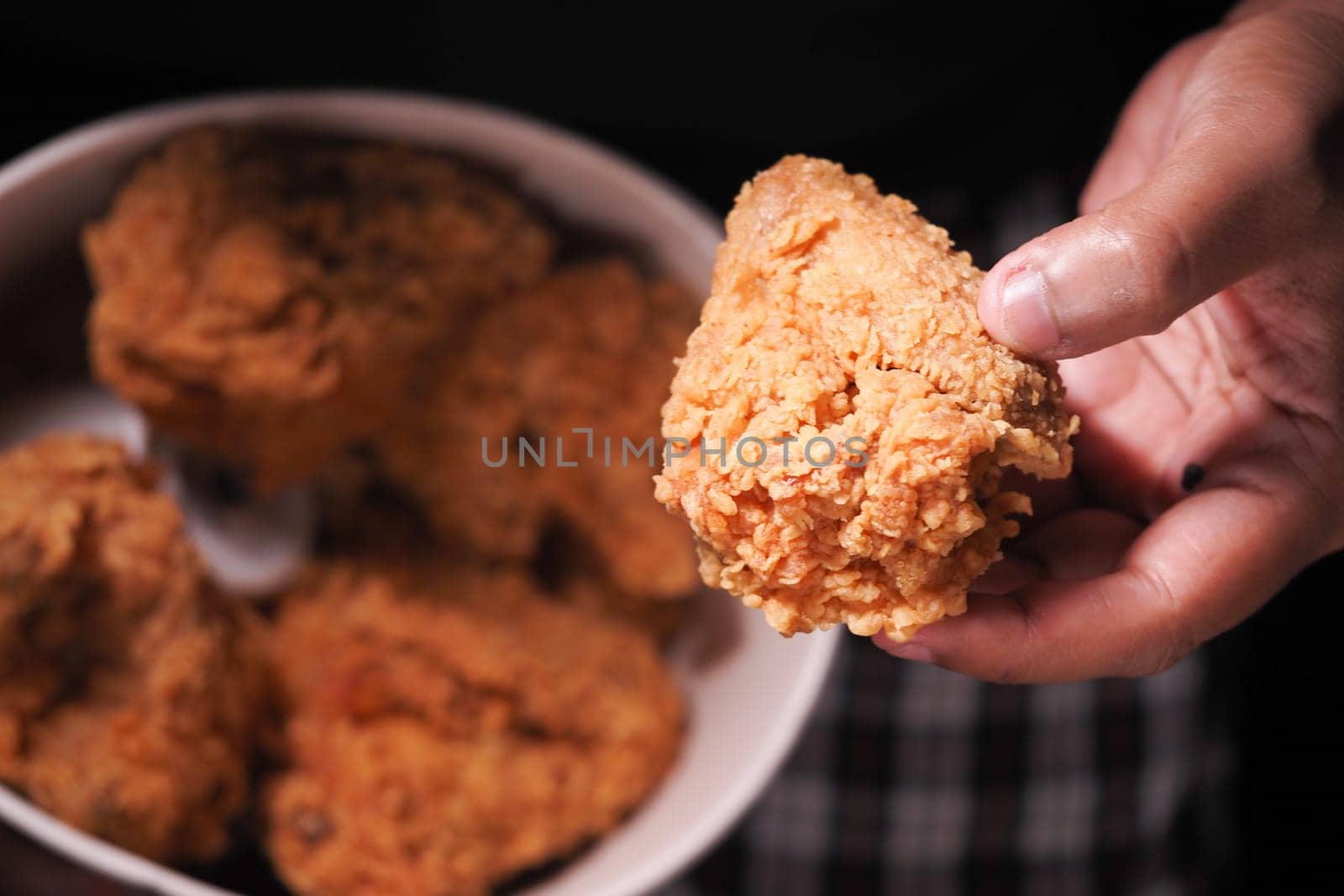 A person holds a piece of fried chicken over a bowl of more.
