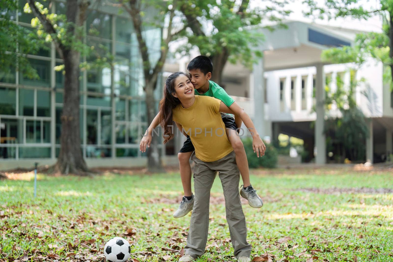 The girl and boy exhibit playful bonding as they enjoy a piggyback ride, a soccer ball rests close by, hinting at their love for outdoor activities.