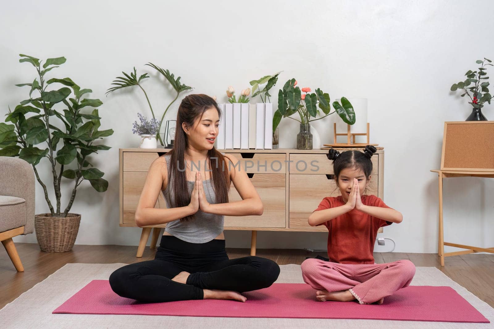 In a serene home setting, a mother and daughter engage in yoga, harmonizing their breath and fostering a deeper bond through shared mindfulness and playful interaction.