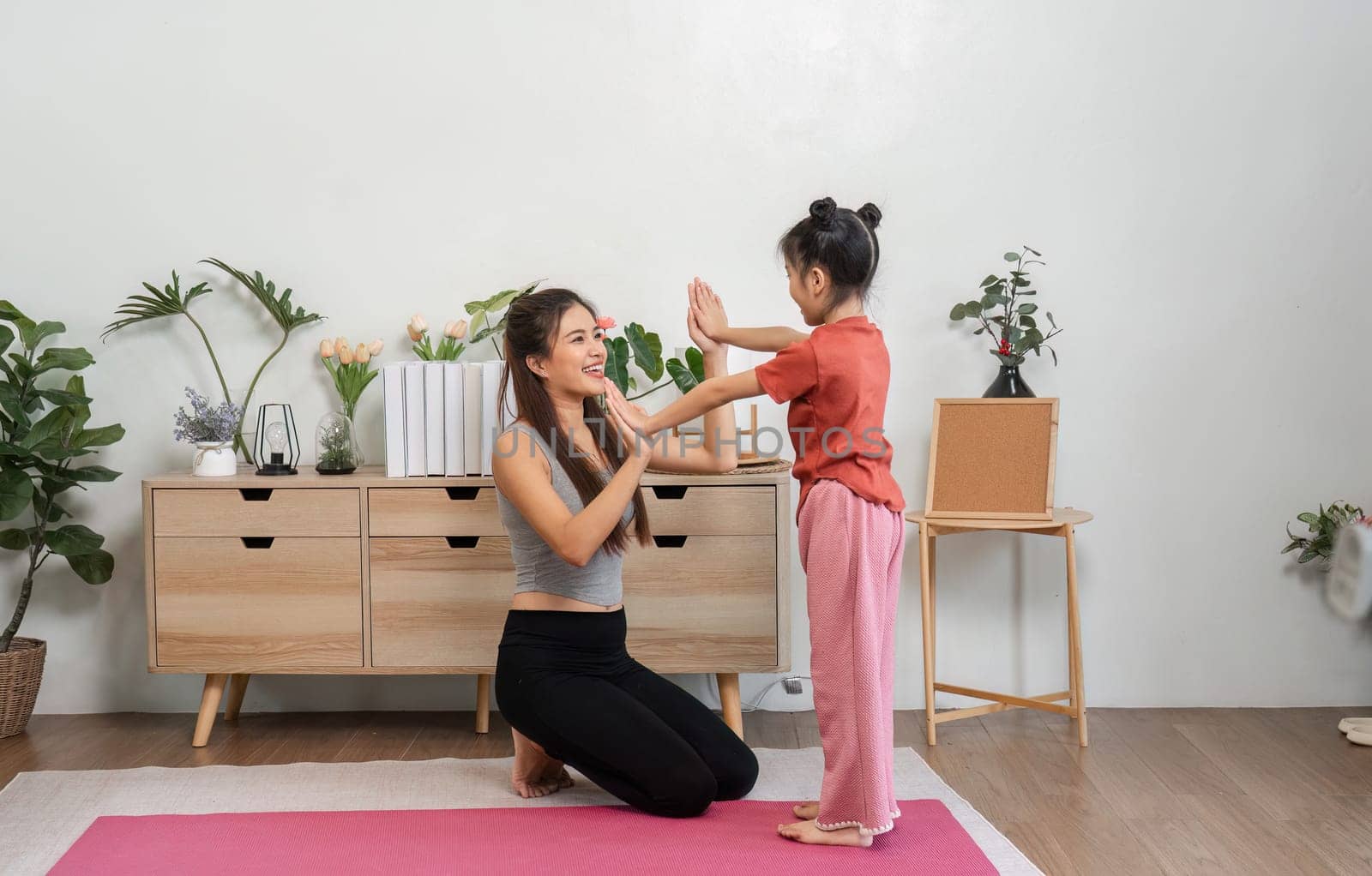Through smiles and laughter, a mother and daughter enjoy their yoga practice, reinforcing family bonds and healthy living.