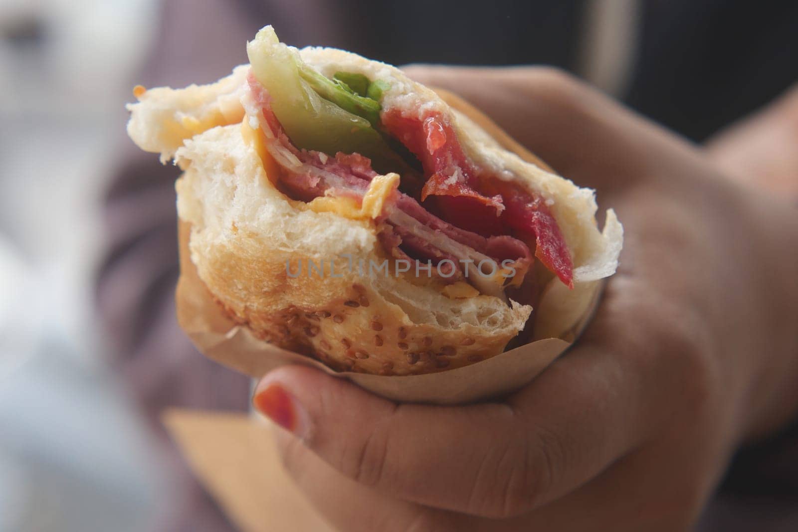 A person enjoys a vibrant sandwich packed with meats and vegetables.