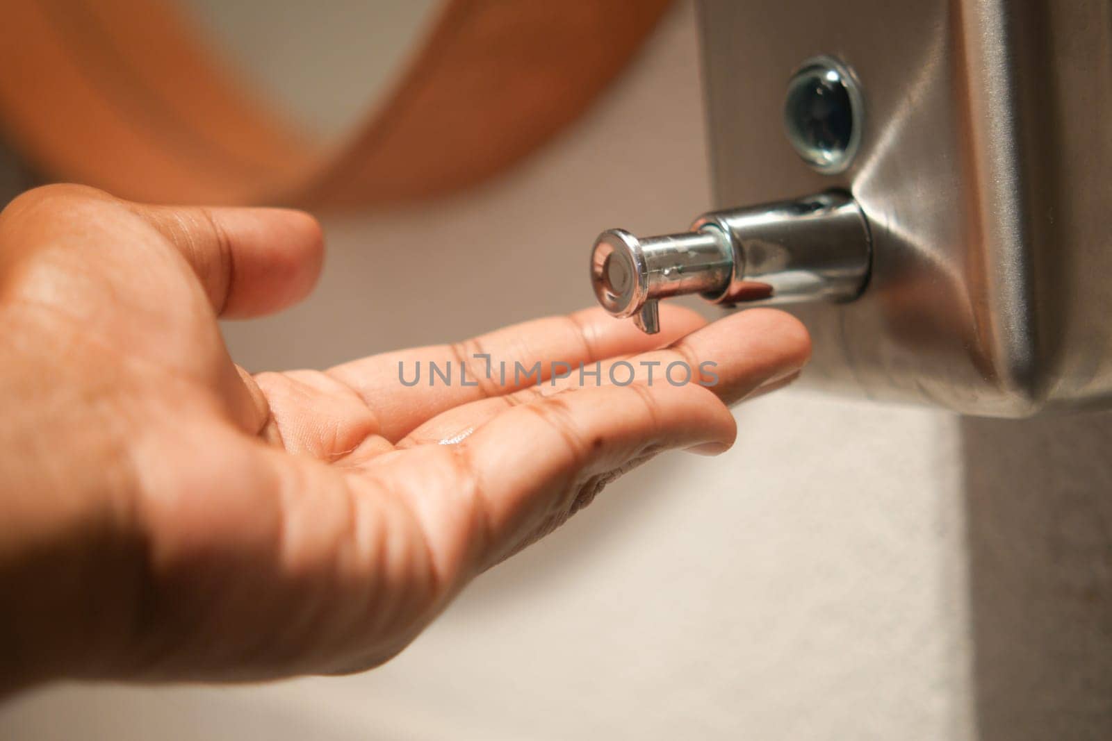 A hand extends toward a faucet in a public restroom, seeking water.