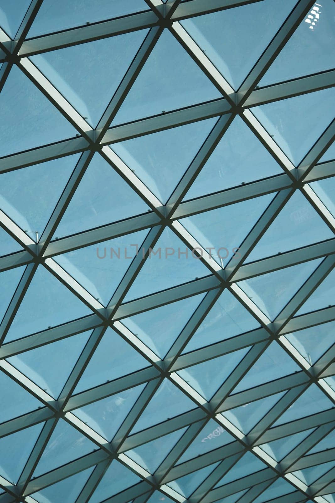 Bright blue sky seen through a geometric glass ceiling during daylight.