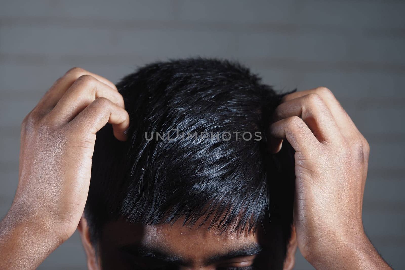 A young man appears stressed, gripping his hair with both hands indoors.