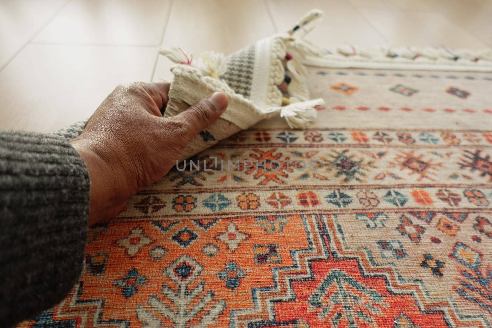 A person smooths a vibrant rug on a polished wooden floor carefully.
