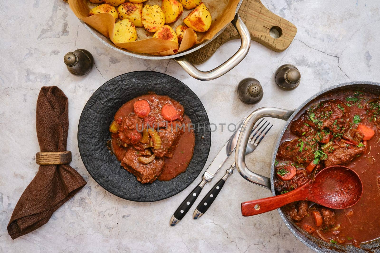 Tender beef stew filled with vegetables is plated on a dark dish, accompanied by a side of seasoned roasted potatoes.