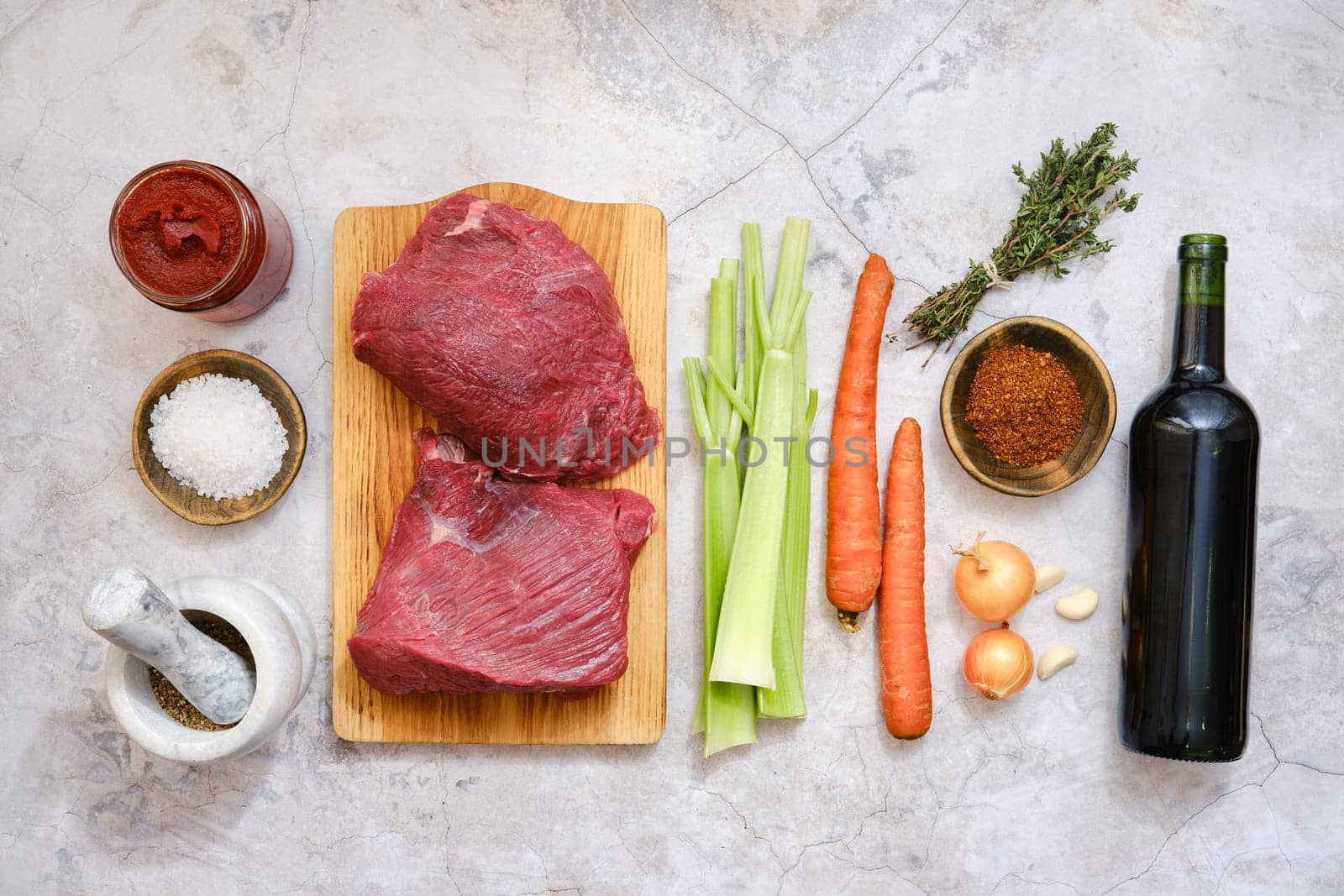 Various fresh ingredients on a kitchen counter, ready for making a beef stew. The setting includes beef meat, vegetables, spices, and a bottle of red wine, inviting culinary creativity.