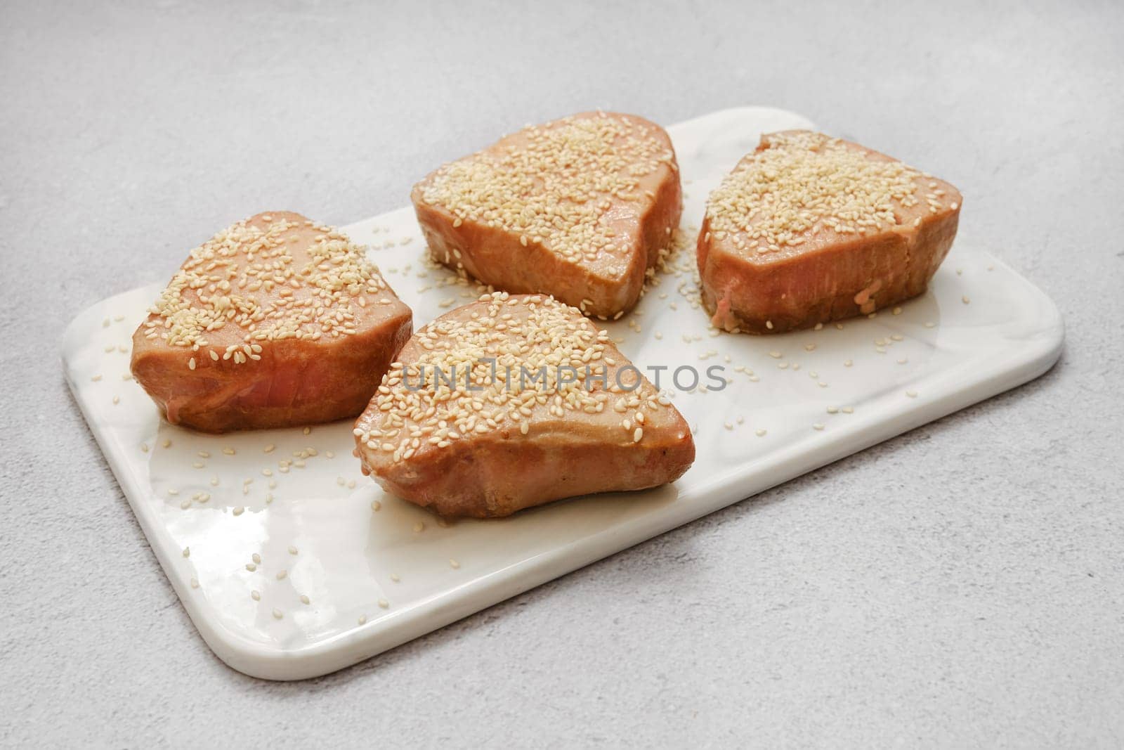 Four tuna steaks topped with a generous layer of sesame seeds are arranged on a marble cutting board.
