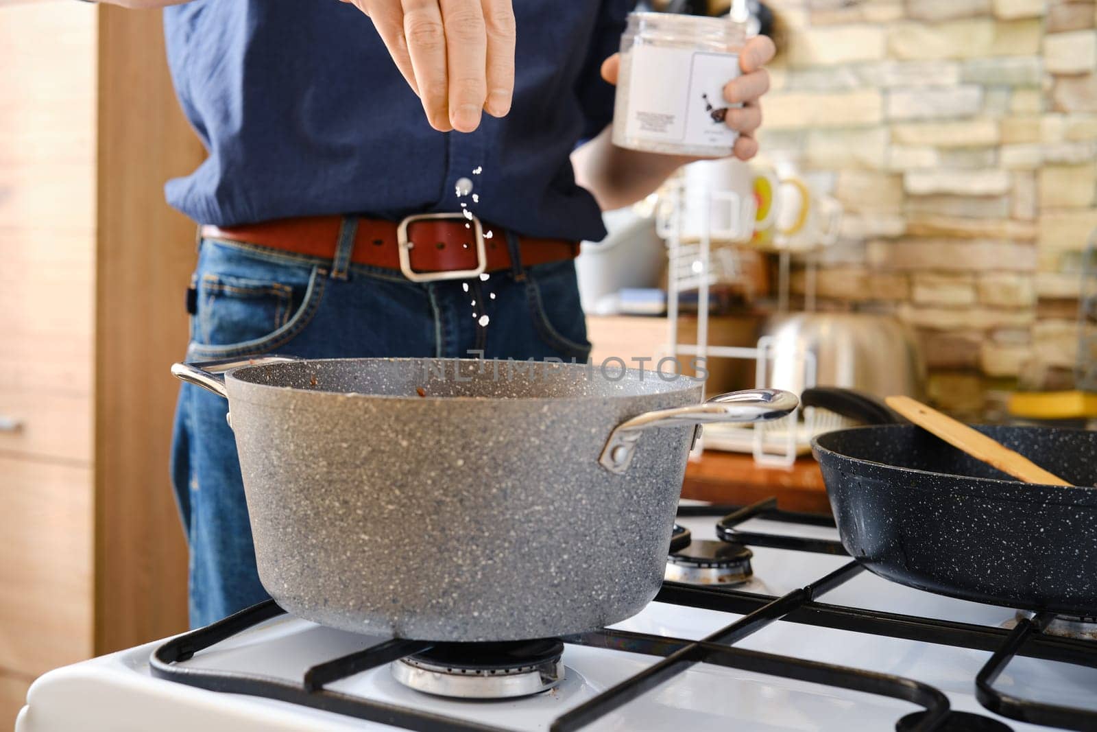 A person is adding sea salt into a pot on a gas stove in a modern kitchen