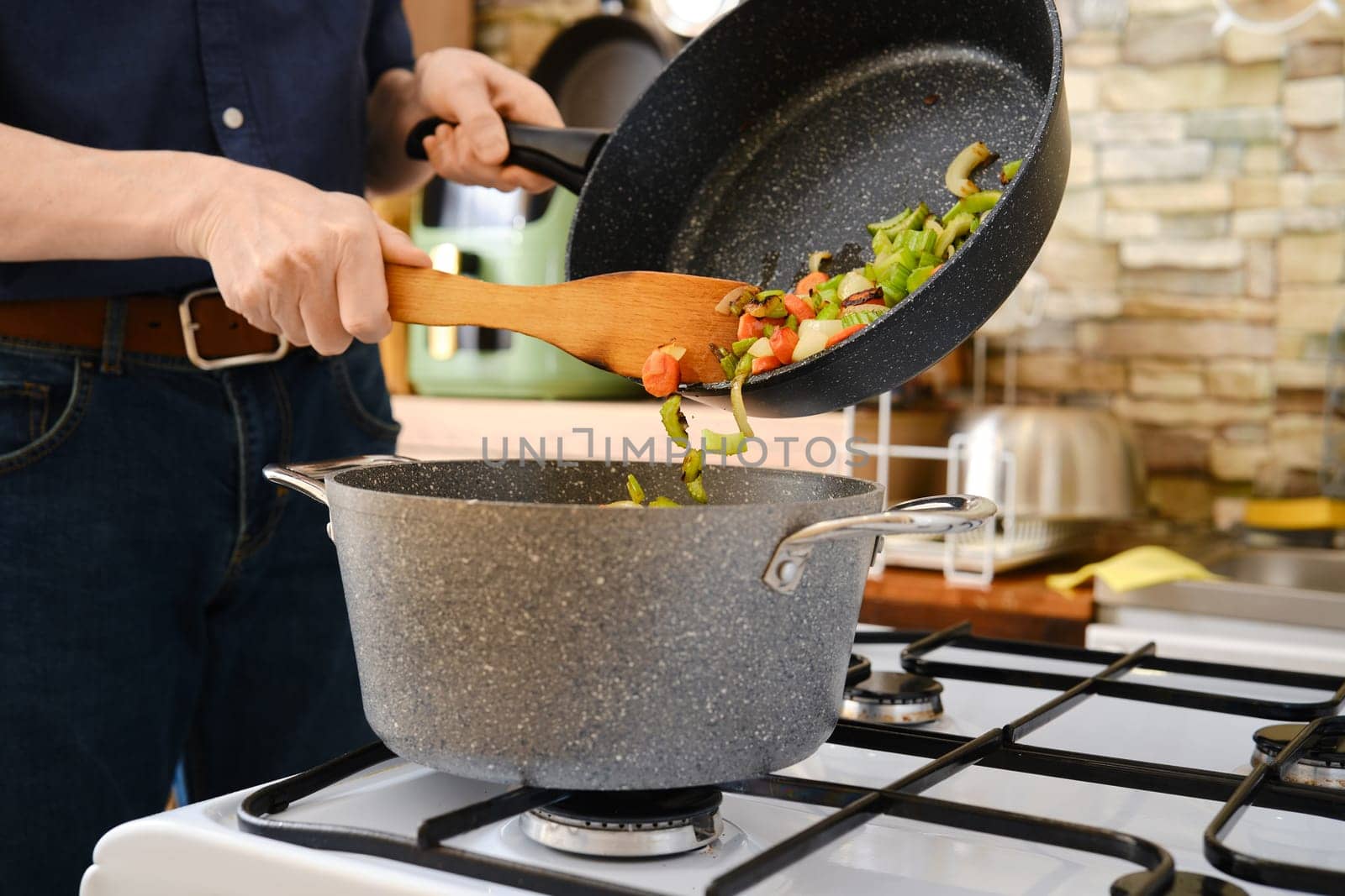 Unrecognizable person shifts stir-fried vegetables into the pot from a frying pan on the stove