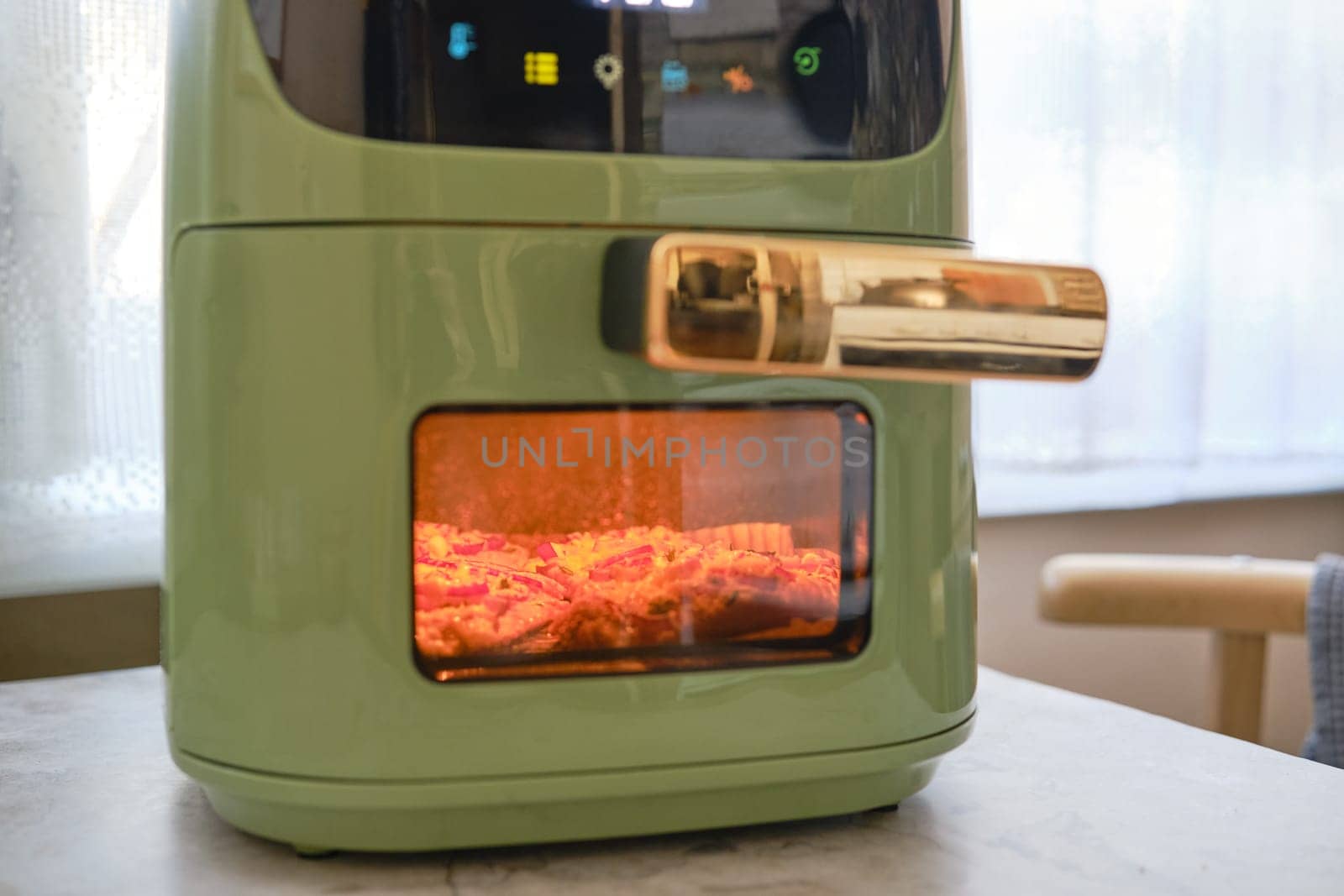 A fresh pork chop is being cooked in an air fryer, showcasing its sleek green design. The appliance features a bright display and transparent window, allowing a view of the delicious meal inside.