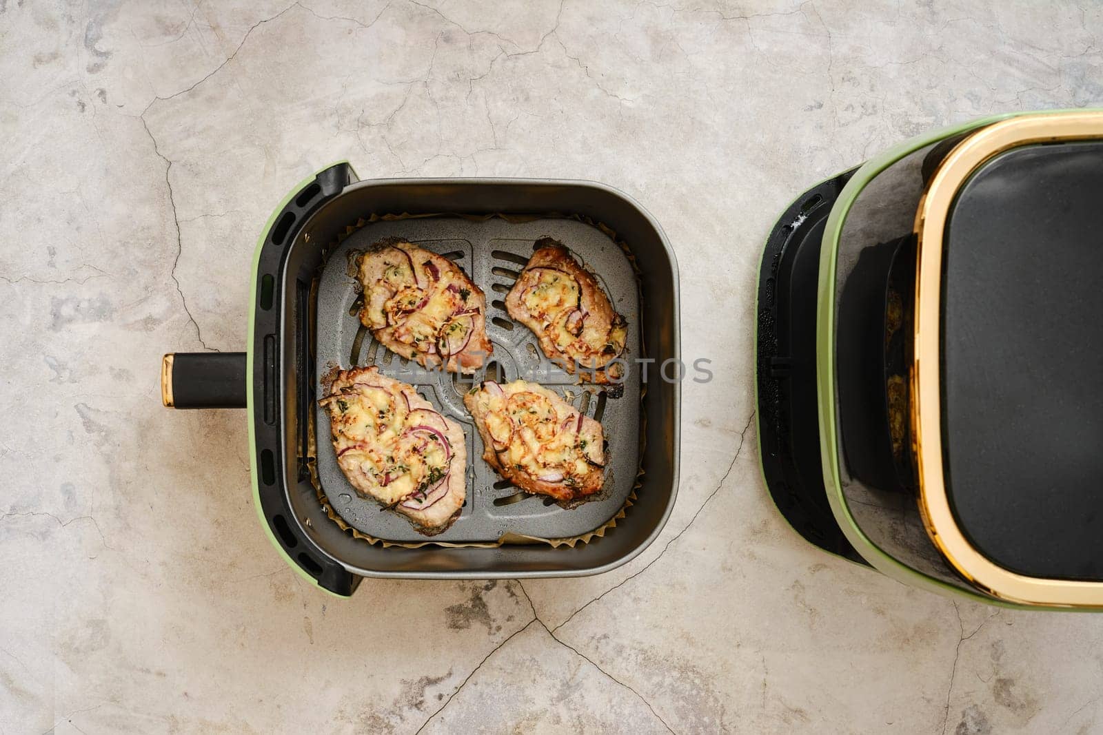 Slices of seasoned pork chop cooking in an air fryer on the kitchen countertop. The juicy meat shows a golden brown crust and ready for plating.