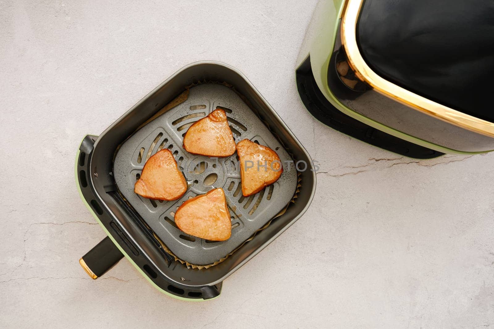 Juicy tuna steaks in a basket of an air fryer, where they are being cooked. The countertop features a clean, minimal design with soft colors and a refined aesthetic.