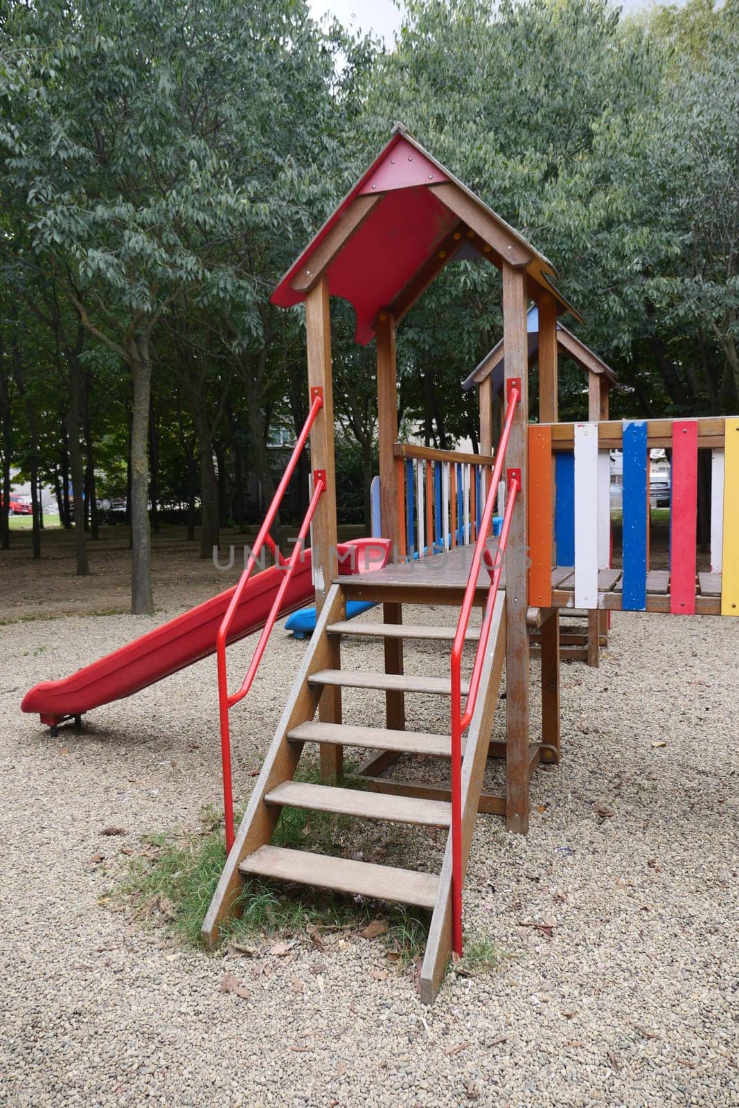 Wooden playground with a slide and vibrant colors surrounded by trees.