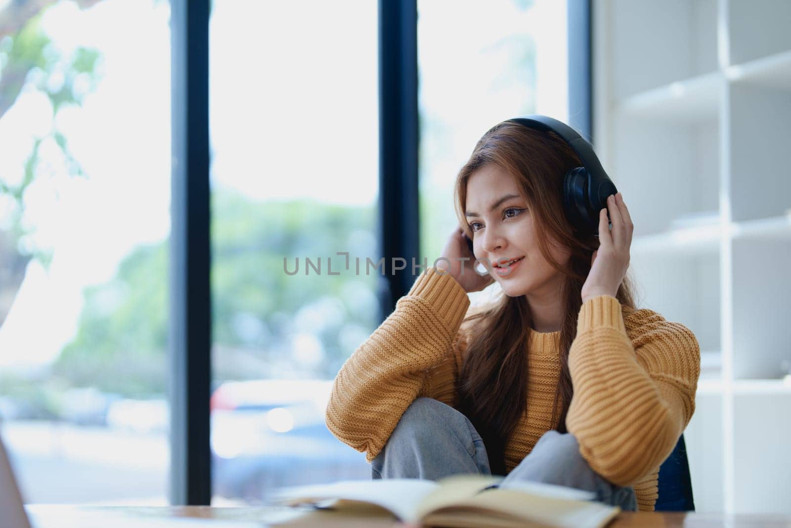 Young woman enjoying a relaxing music break at her desk while using headphones, writing in a notebook, and working on her laptop for calm inspiration.