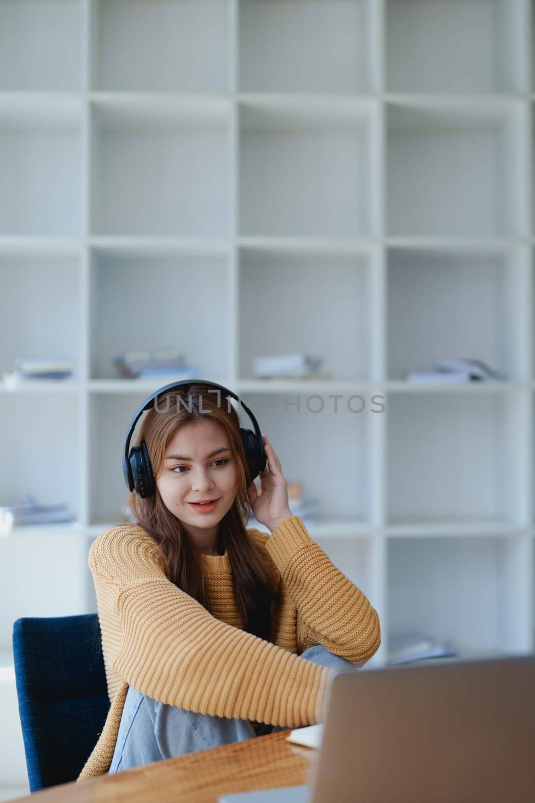 Young woman enjoying a relaxing music break at her desk while using headphones, writing in a notebook, and working on her laptop for calm inspiration.