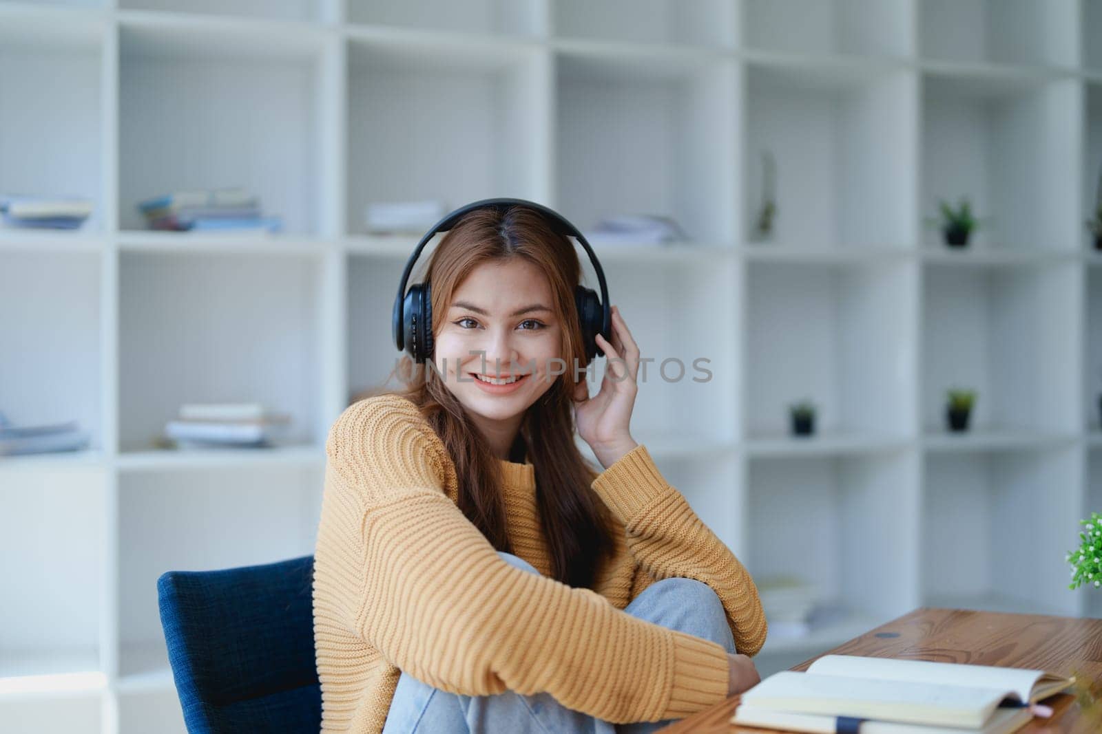 Young woman enjoying a relaxing music break at her desk while using headphones, writing in a notebook, and working on her laptop for calm inspiration.