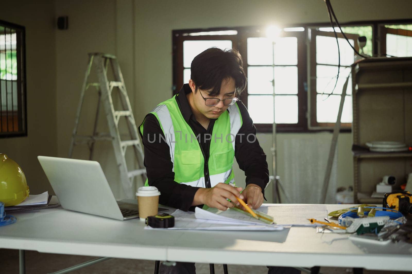 Architect reviewing building plans with measuring tools on a busy workspace.