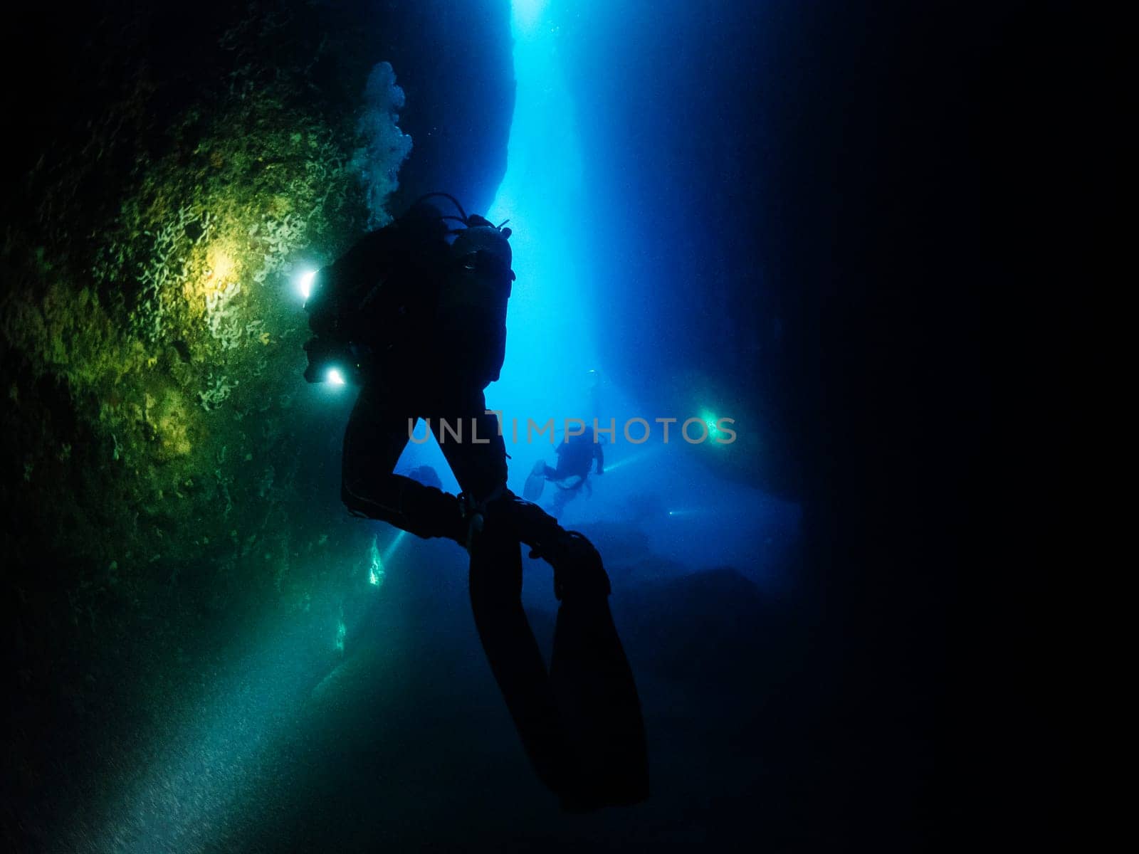 group of scuba divers diving inside a marine cave that they illuminate with their flashlights, concept of active leisure lifestyle and underwater adventure