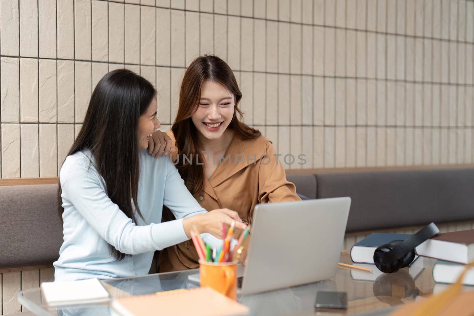 Two female students huddle around a laptop, sharing insights and enjoying a light hearted moment during their academic session.