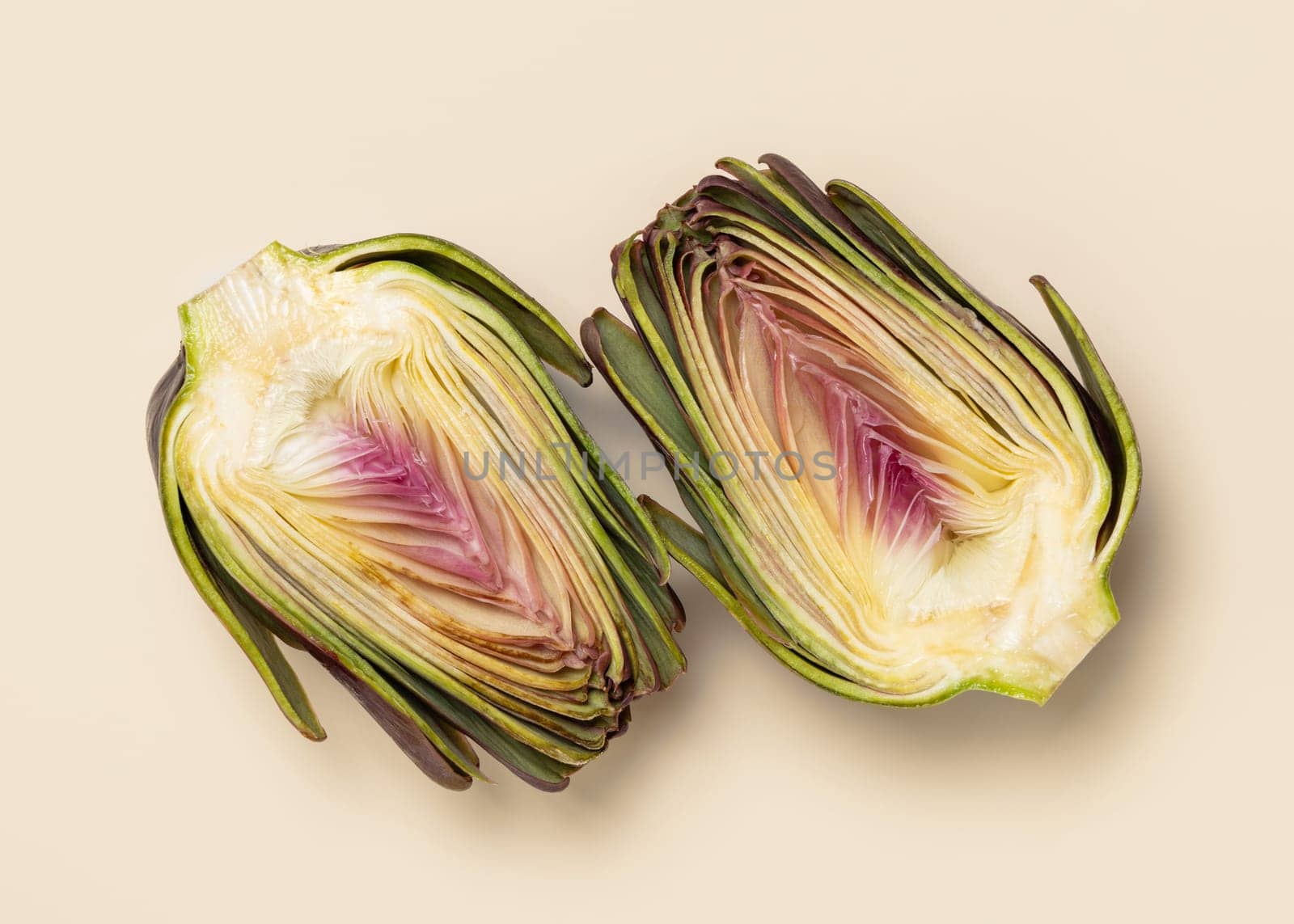 Cut raw purple artichokes on light yellow background top view. Fresh vegetables from farmers market ready to cook, vegetarian diet. Italian cousine ingredient